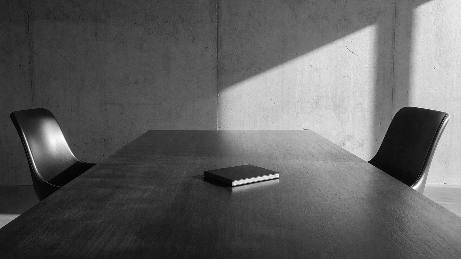 Mesa de reunión con dos sillas vacías y un cuaderno cerrado